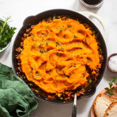 pan with healthy sweet potato shepherd's pie on white background with spices and bread