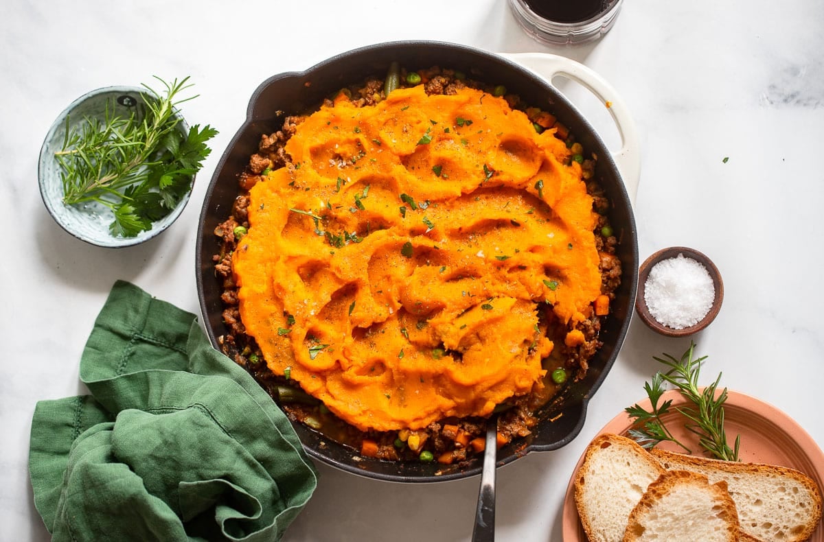 pan with healthy sweet potato shepherd's pie on white background with spices and bread