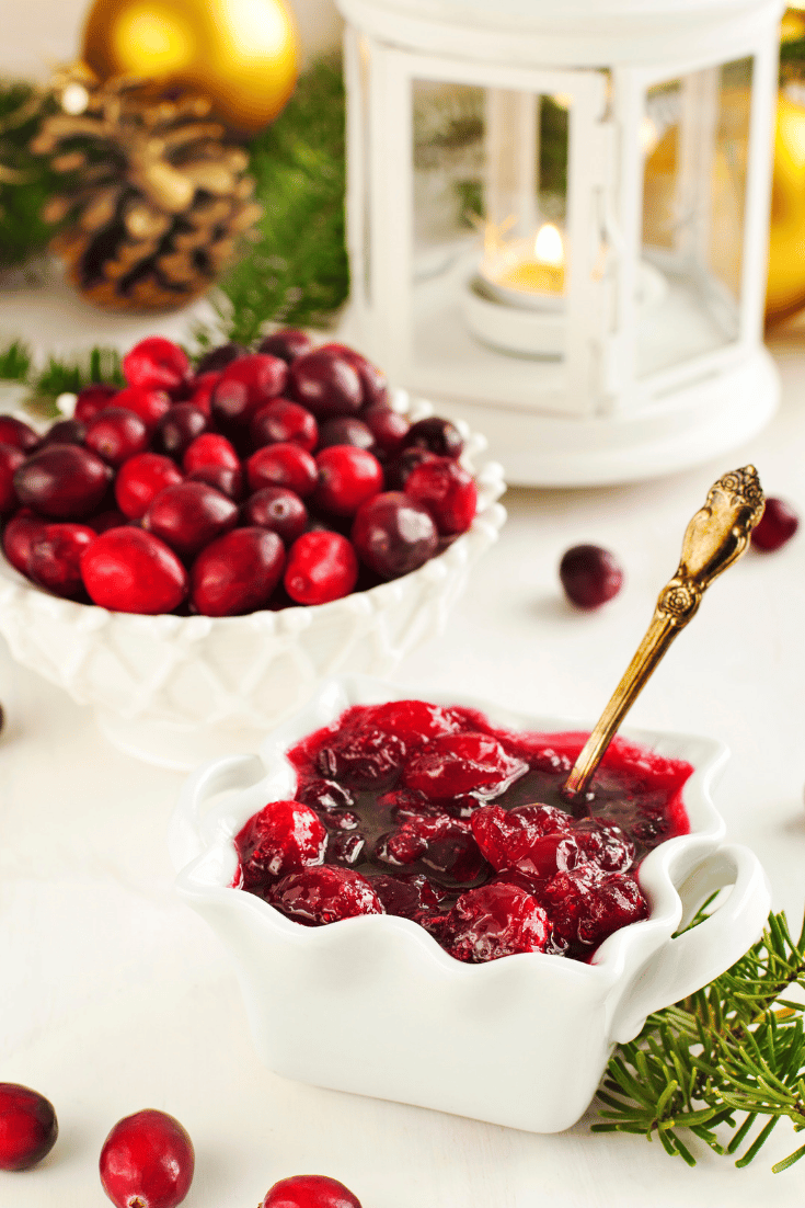 Bowl of homemade cranberry sauce with gold spoon and bowl of uncooked cranberries in background