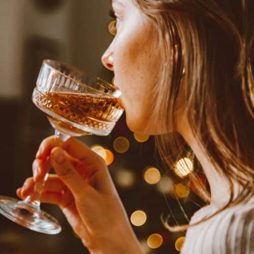 woman drinking holiday drink with lights behind her