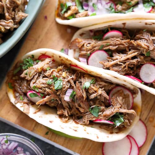 Pork carnitas in flour tortillas with sliced radishes and on wood cutting board