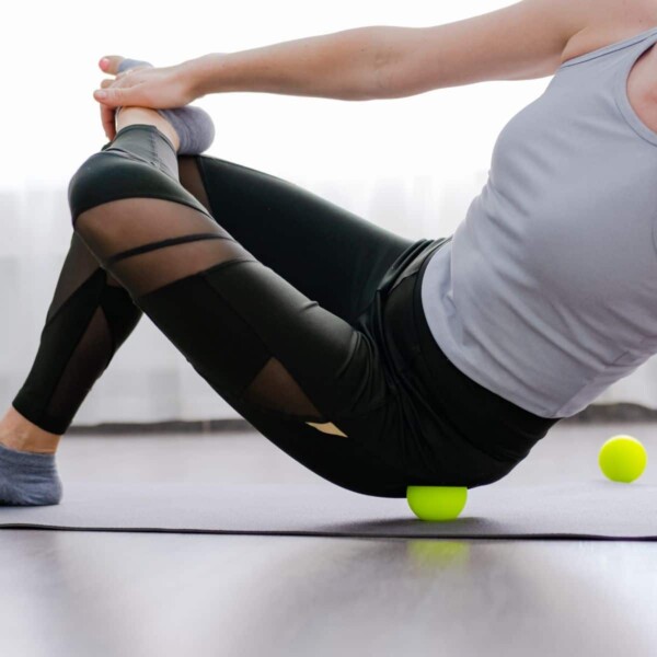 woman exercising hip muscles rolling on small ball at gym