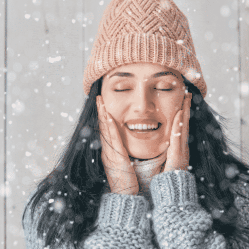 Woman touching cheeks in the snow for a post on winter skin care