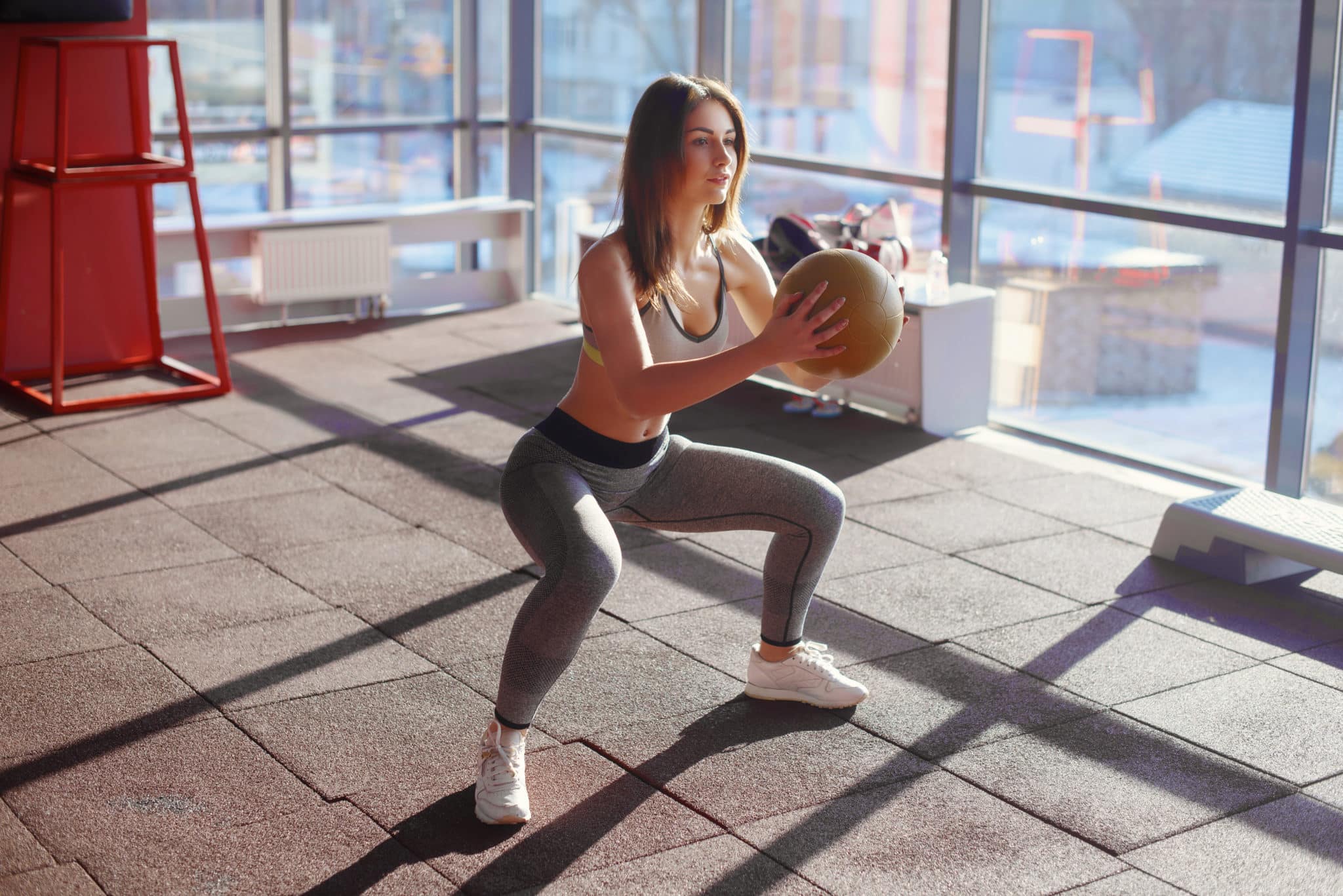 Young woman in apartment doing a squat with medicine ball