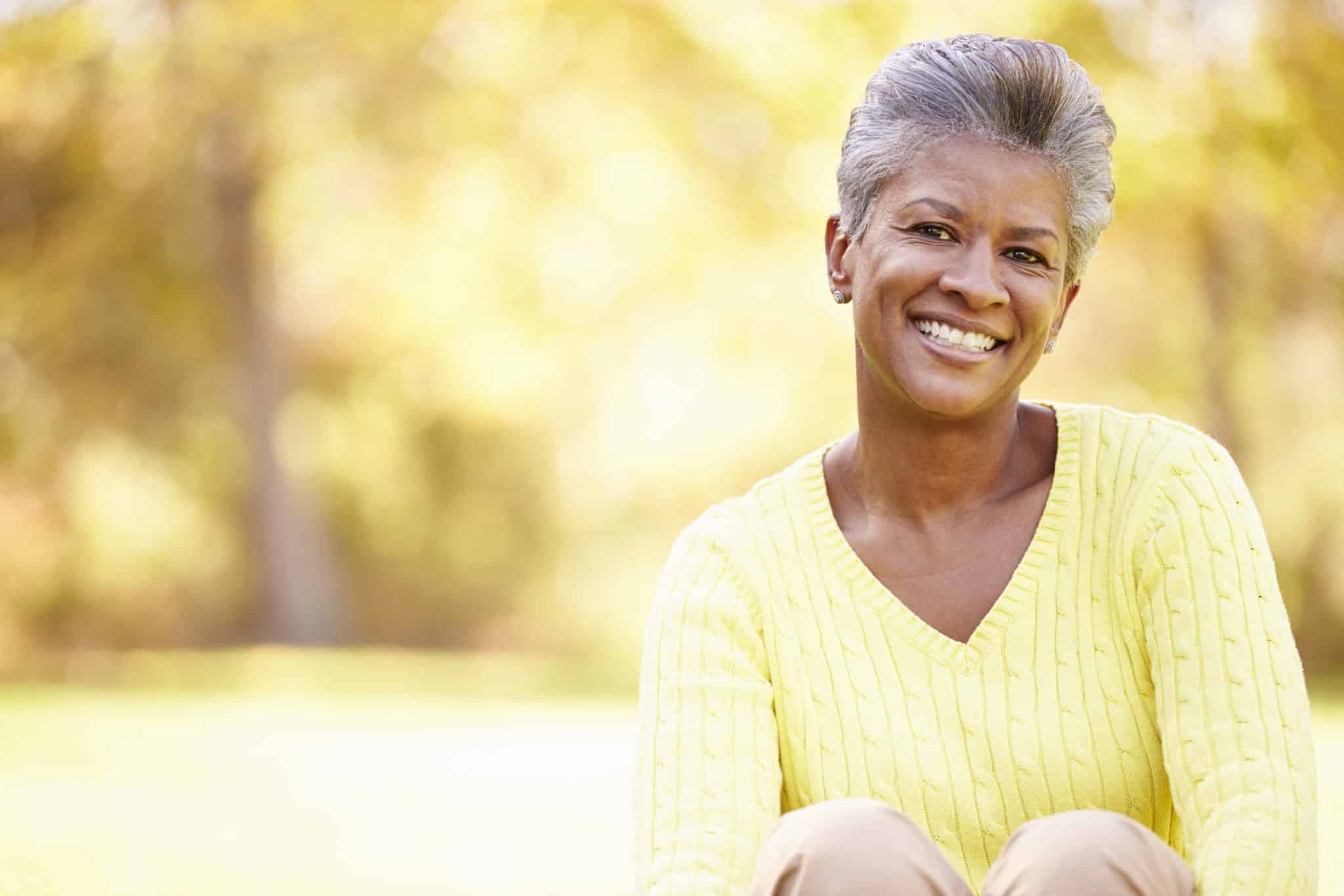 woman over 50 smiling outdoors in yellow sweater