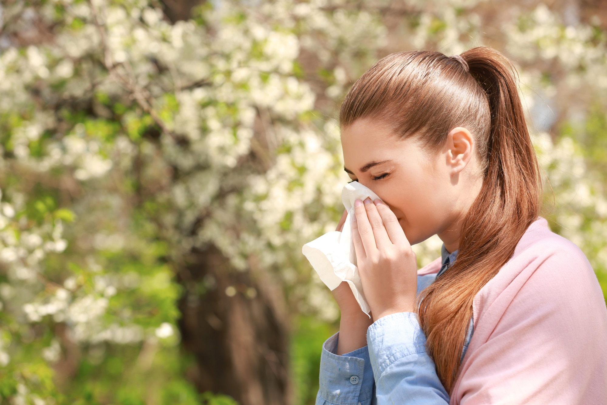 Young woman outdoors sneezing into a tissue.