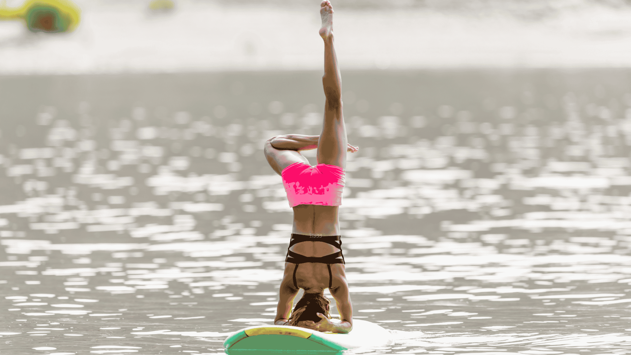woman doing headstand on paddle board in pink shorts