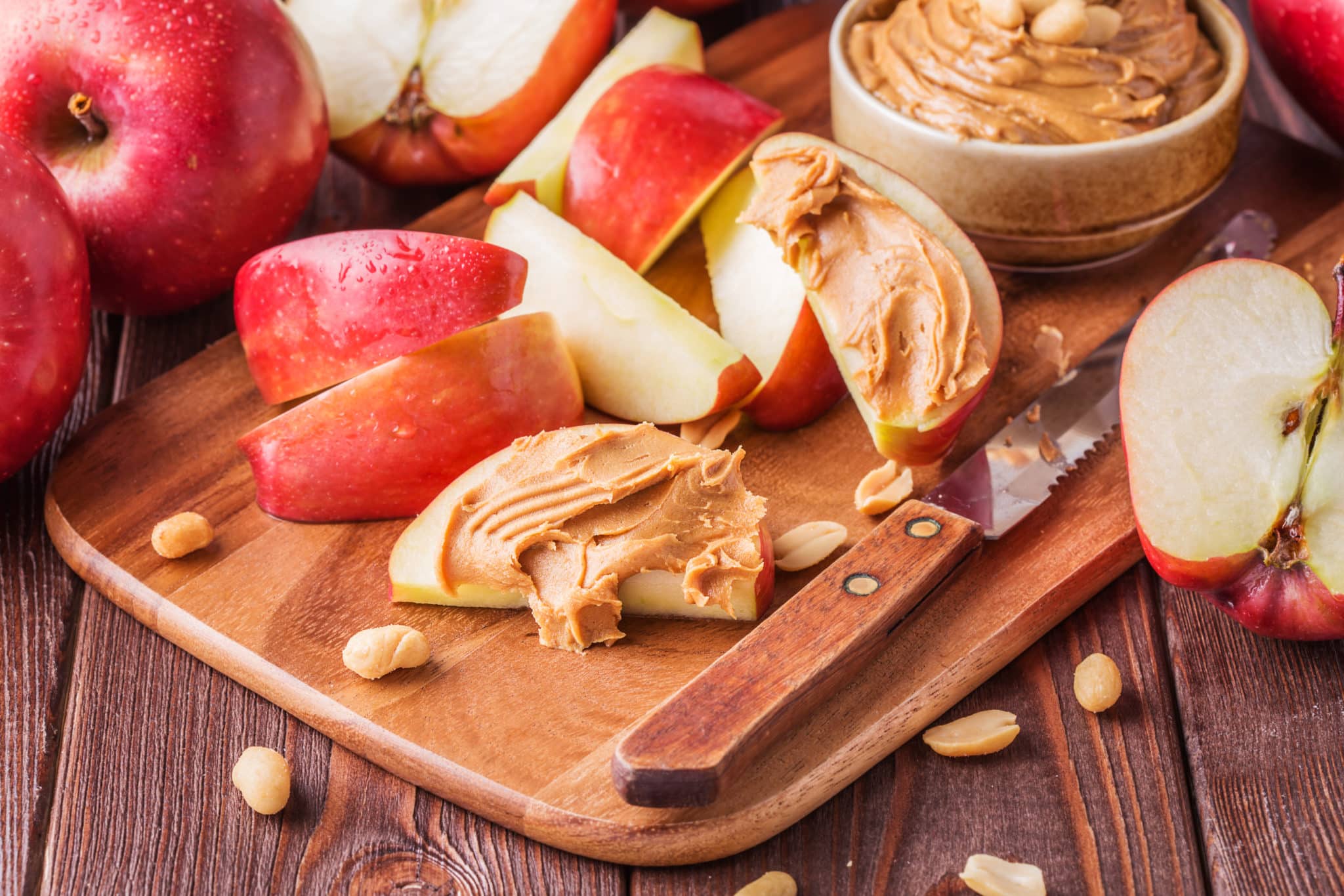 Sliced apples with peanut butter on cutting board with knife