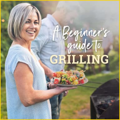 Middle aged woman holding plate of kebobs in front of the grill