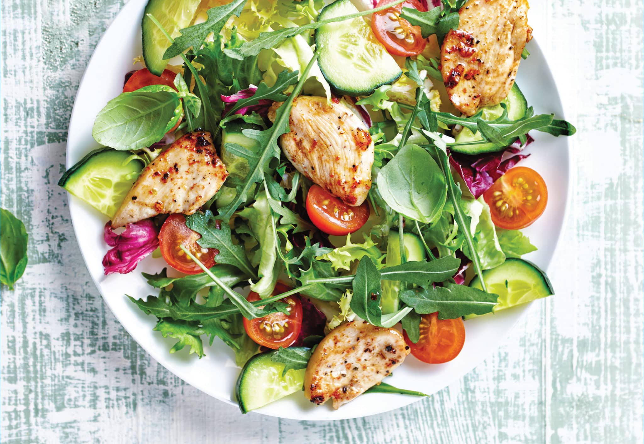 Green salad in white bowl with chicken, tomatoes and cucumber