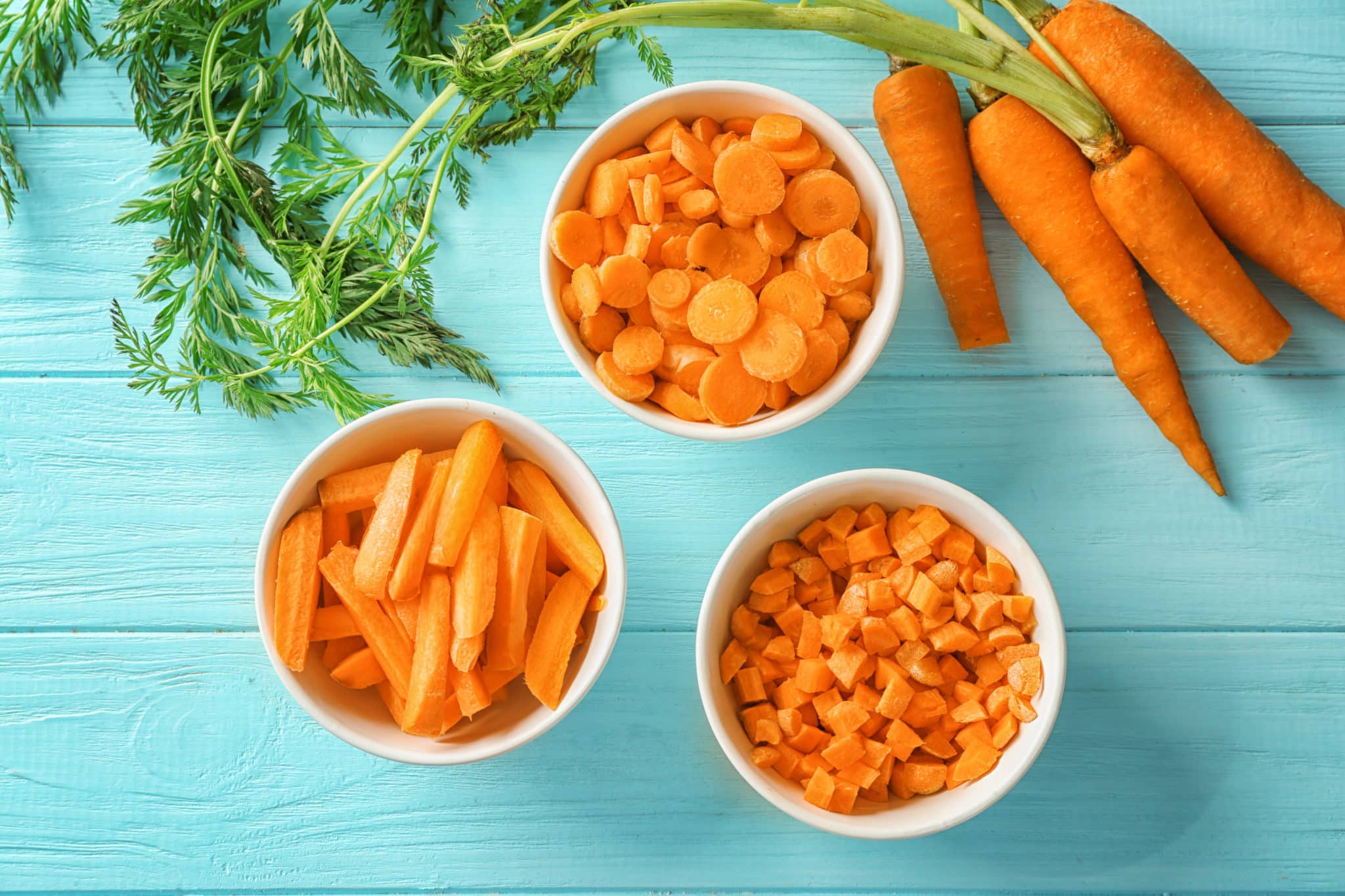 Bowls of carrots cut in different shapes on teal blue table