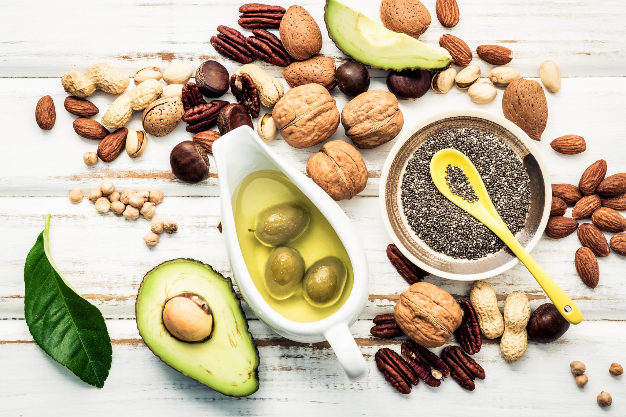 Various healthy fats on white including olive oil, avocado, chia seeds and nuts
