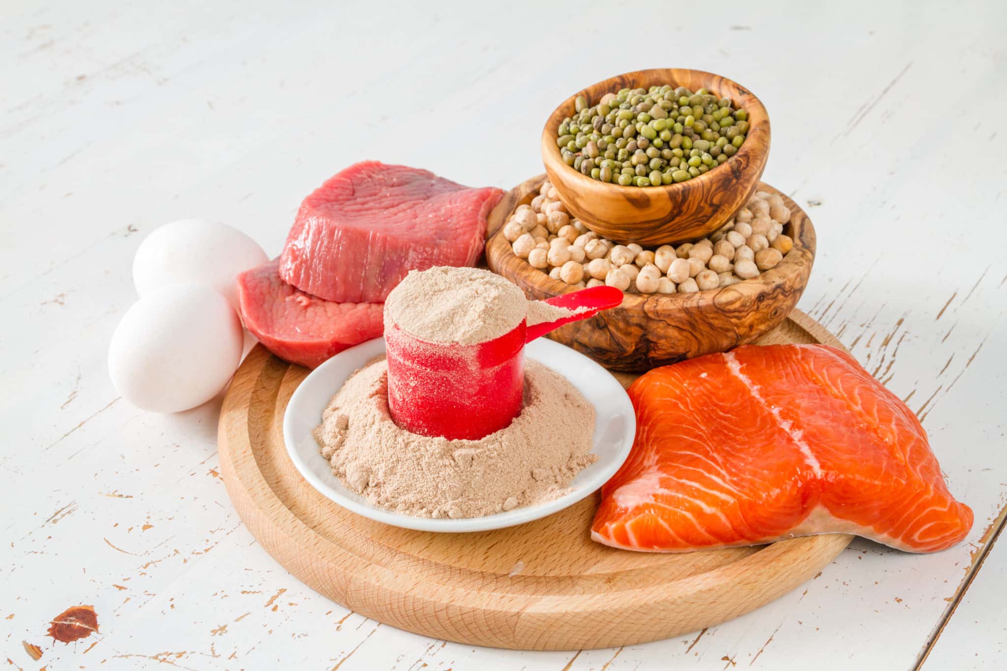Various proteins on wooden platter including protein powder, salmon, pork, lentils and eggs