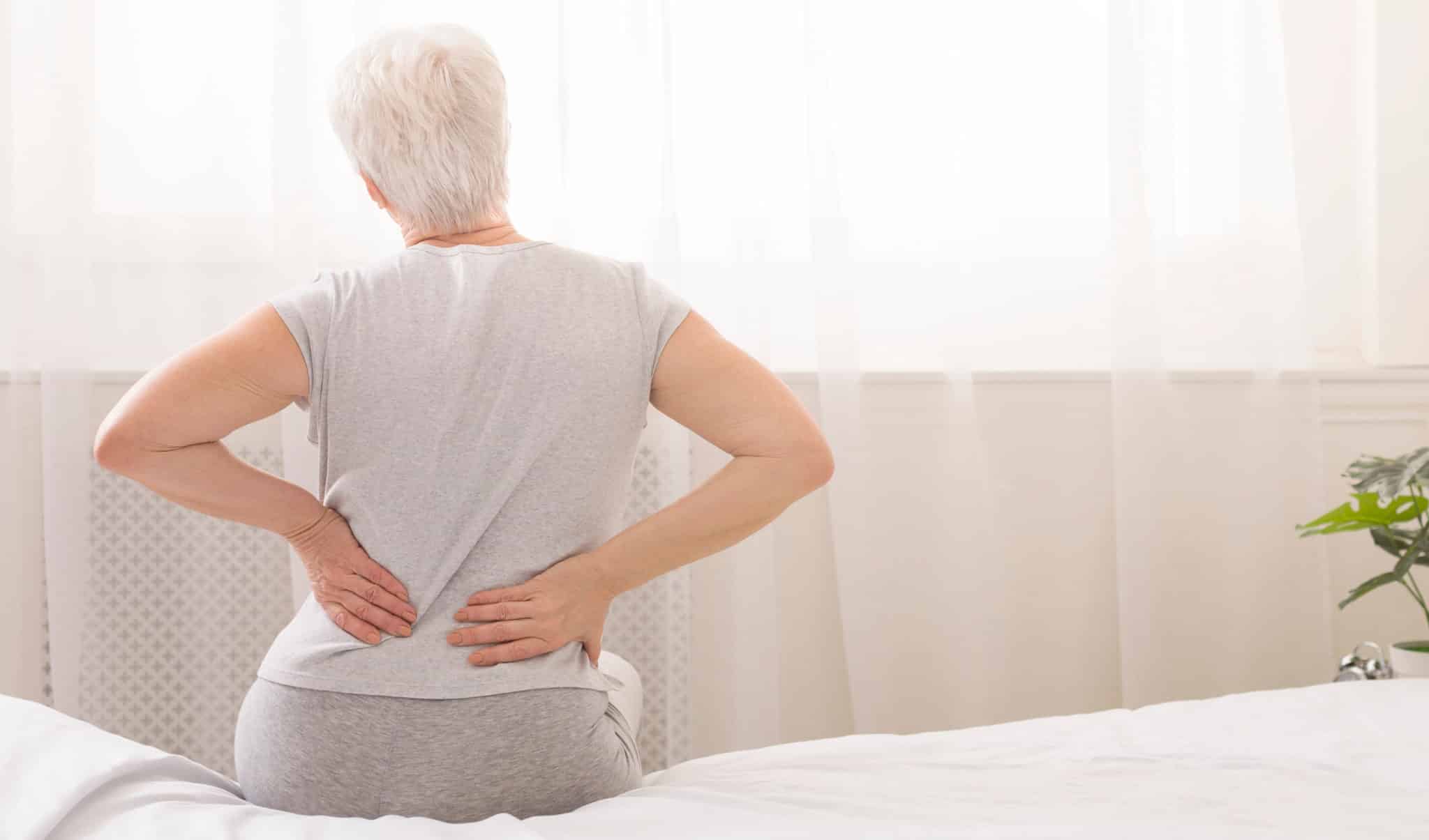 Woman sitting in bed with hands on back from pain