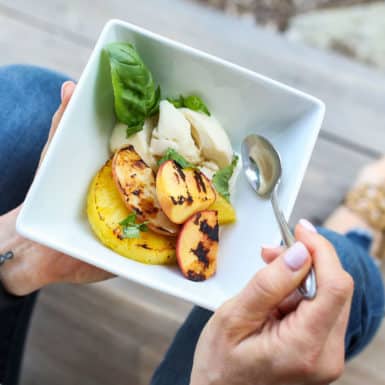 A bowl of grilled peaches and pineapple with ice cream and basil