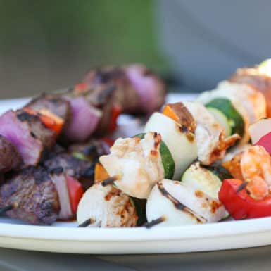 Kabobs skewers with chicken, beef shrimp and vegetables on a white plate