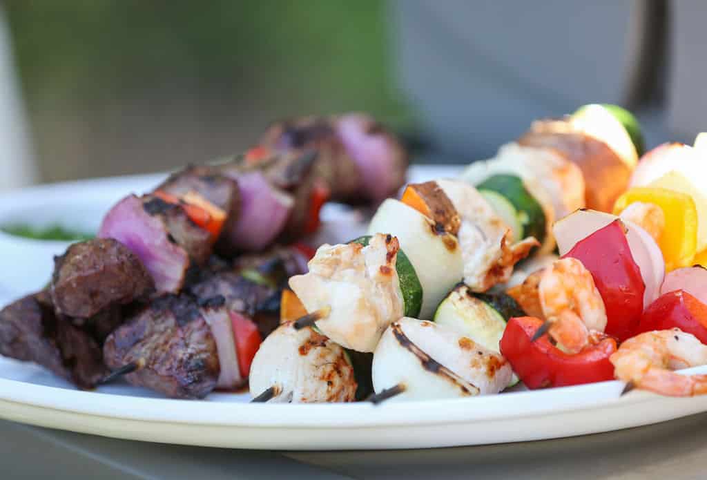 Kabobs skewers with chicken, beef shrimp and vegetables on a white plate