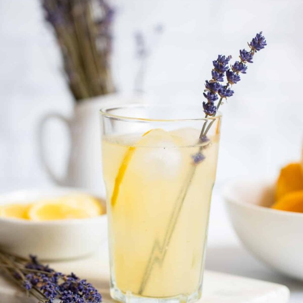 glass lavender lemonade with ice garnished with lemon slice and sprig of fresh lavender.