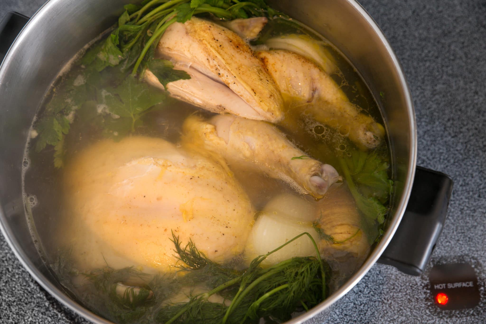 Chicken in boiling pot of water with herbs