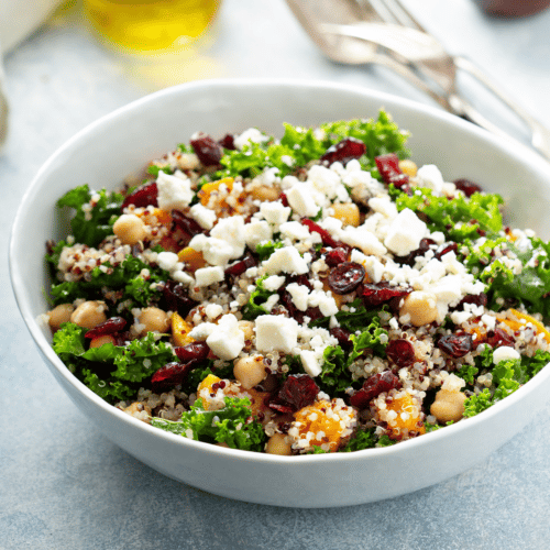 Kale salad in white bowl with butternut squash, goat cheese and dried cranberries