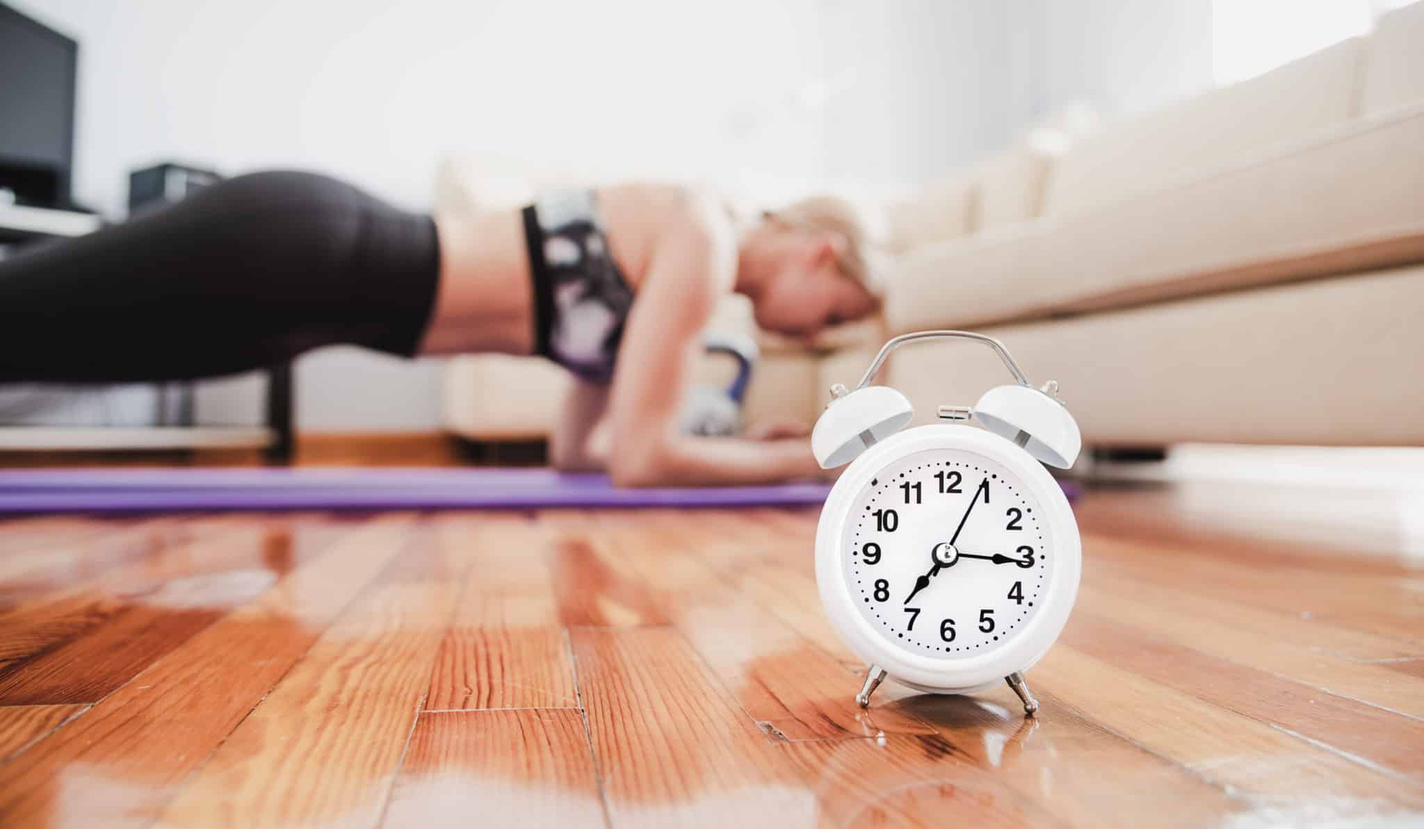 Young woman holding a plank on forearms in living room with clock timer in front