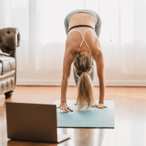 woman with yoga mat doing a workout in her living room with her computer