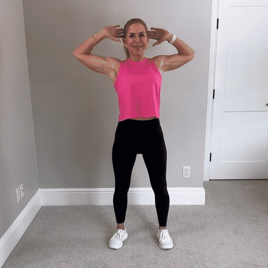 Chris Freytag wearing a pink tank top and black leggings doing a cross body bicycle crunch.