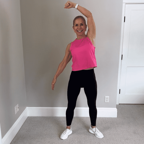 Chris Freytag wearing a pink tank top and black leggings doing a standing oblique crunch. 