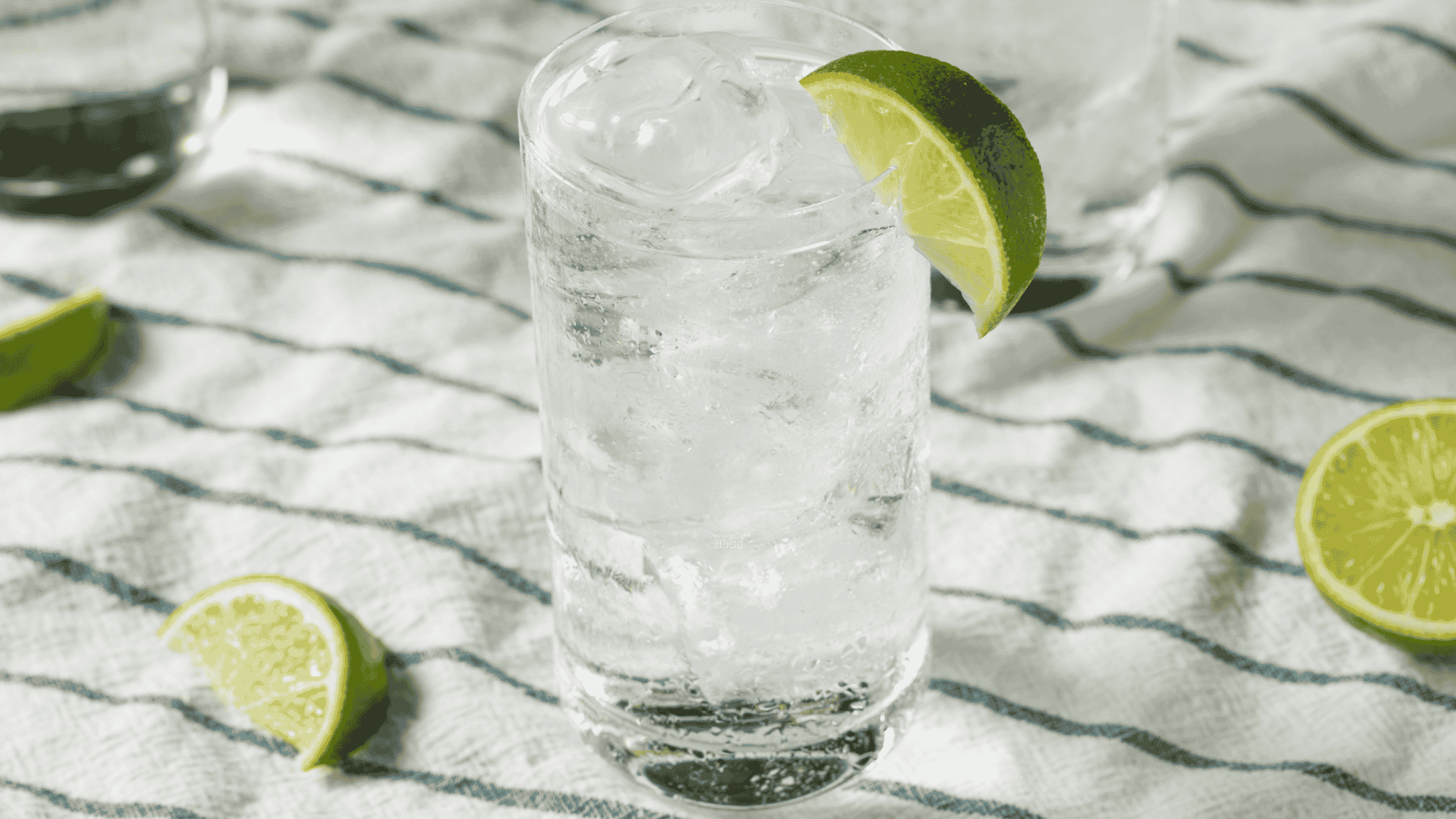 cup of tequila soda on white cloth with limes