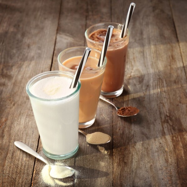 Three glasses of different colored protein powder drinks.