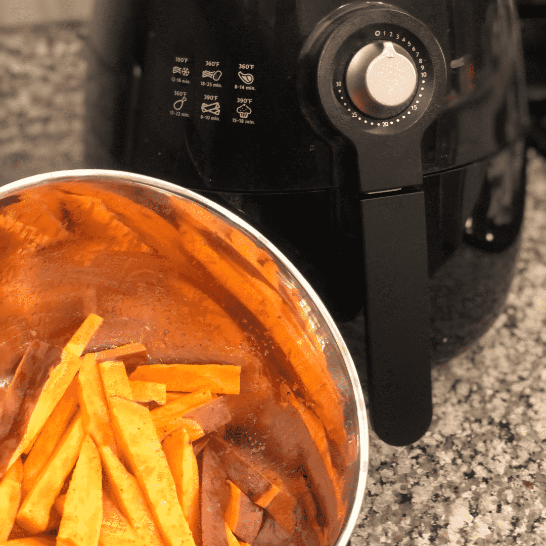Black Philips Air Freyer next to a silver bowl with cut up sweet potatoe fries