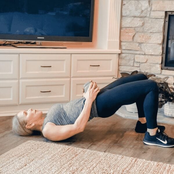 Chris Freytag doing a glute bridge holding a dumbbell on her hips for added weight.