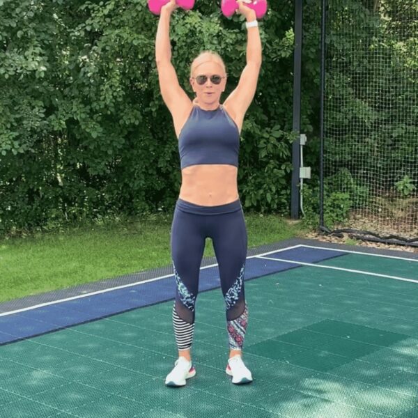 Chris Freytag in a blue athletic crop top holding the top of an overhead dumbbell shoulder press