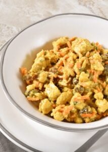 A white bowl of curry chicken salad with raisins and carrots