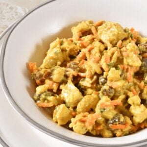 A white bowl of curry chicken salad with raisins and carrots