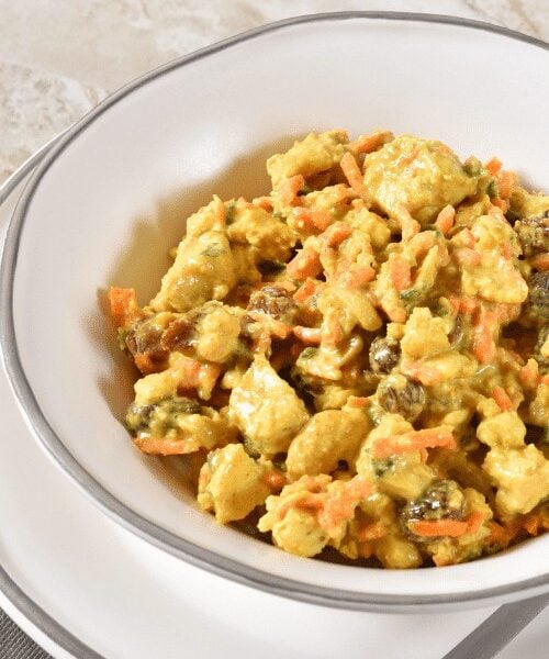 A white bowl of curry chicken salad with raisins and carrots