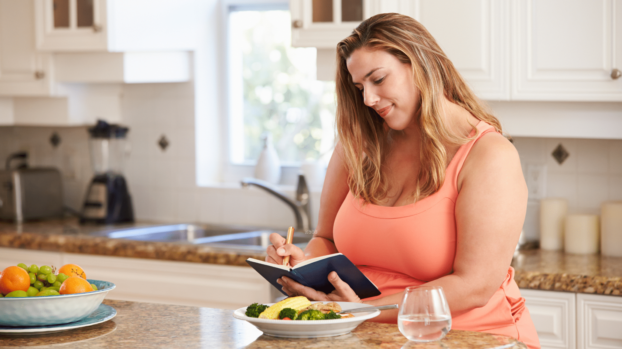 woman writing down progress while eating healthy lunch
