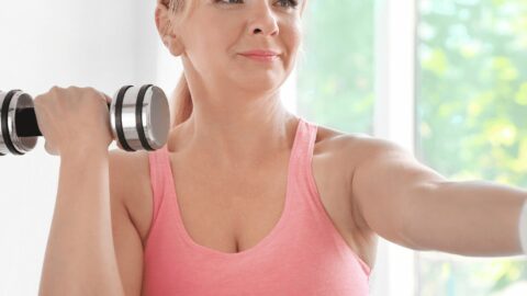 Middle age woman in pink workout top holding dumbbells