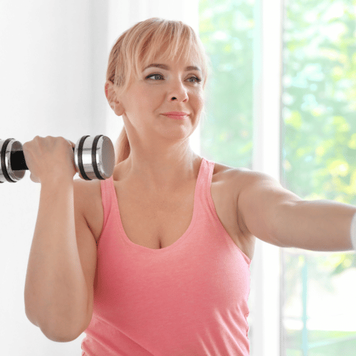 Middle age woman in pink workout top holding dumbbells