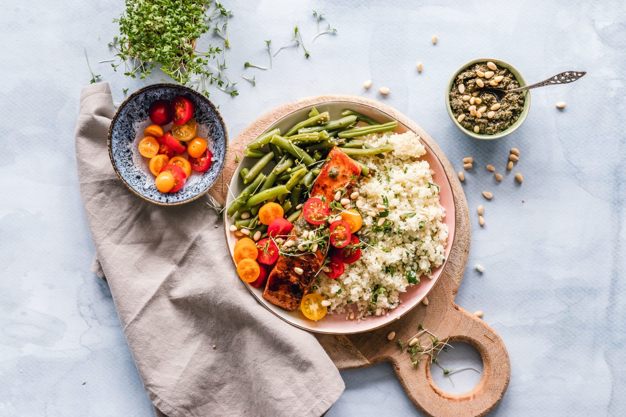 A large bowl of quinoa, salmon, sliced cherry tomatoes, and green beans next to smaller bowls of cherry tomatoes and pesto.
