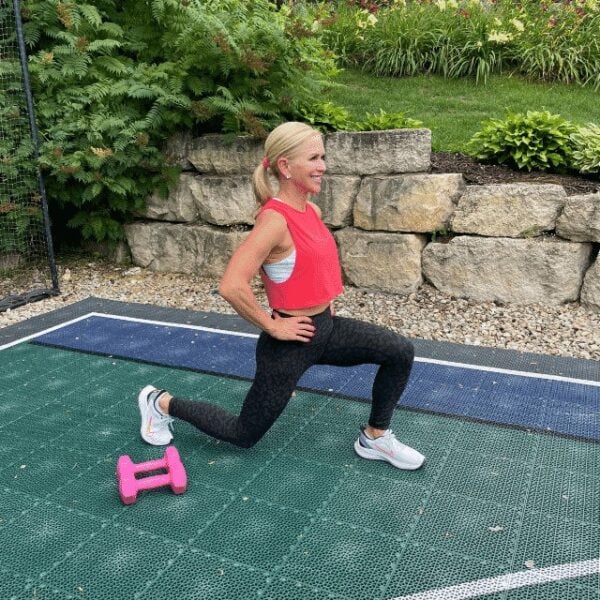 Chris Freytag on a sports court holding a static basic lunge. Pink dumbbells shown in the picture for reference.