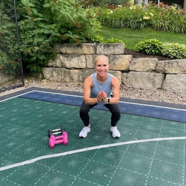 Chris Freytag performing a squat low hold with pink dumbbells to the side.