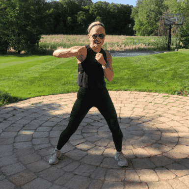 Chris Freytag standing outside, wearing all black fitness outfit. Holding a hook position for a kickboxing tabata workout.