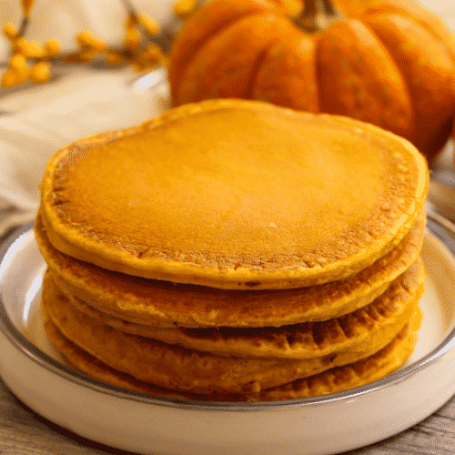 Healthy pumpkin pancakes stacked on a white plate with a pumpkin in the background