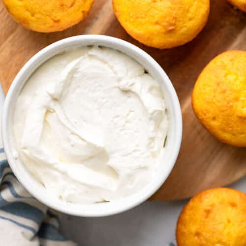 bowl of healthy cream cheese frosting surrounding by yellow muffins