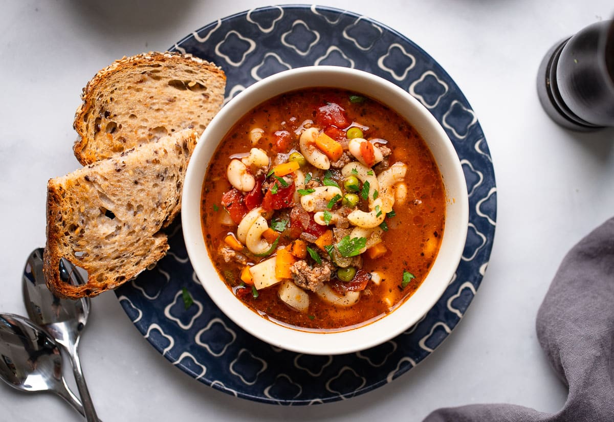 top view of single serving of hamburgers soup on white counter with bread
