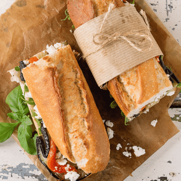 Two bagette sandwiches filled with vegetables on a wooden board