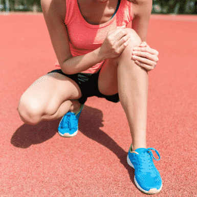 woman in workout clothing holding her knee in pain on a track