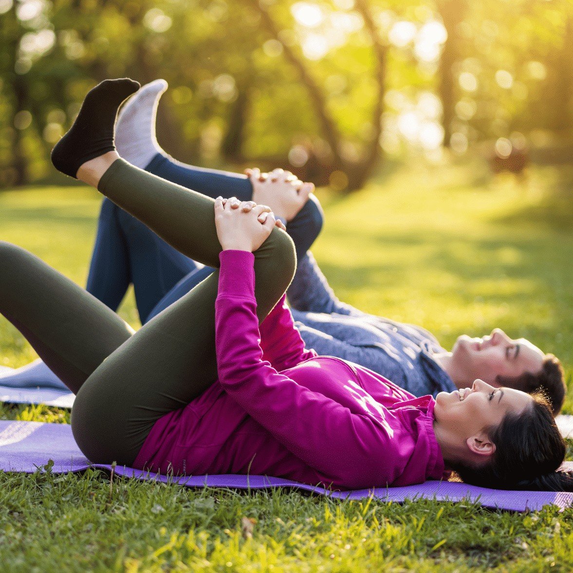 man and woman laying on mats in the park strech