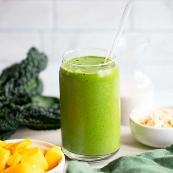 green smoothie in glass with straw in white kitchen surrounded by ingredients